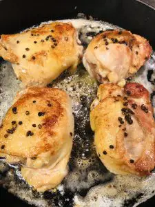 Browned Chicken thighs seasoned with coarse pepper frying in butter in a cast iron skillet