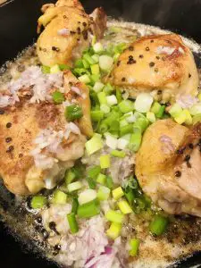 Browned chicken thighs in a cast iron skillet topped with chopped green onions and diced shallots