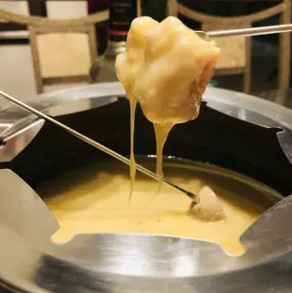 bread on a fondue fork dipped in cheese from a fondue pot