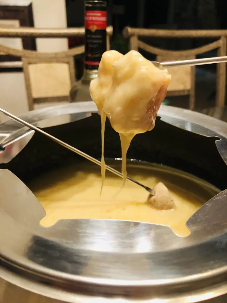 bread on a fondue fork dipped in cheese from a fondue pot