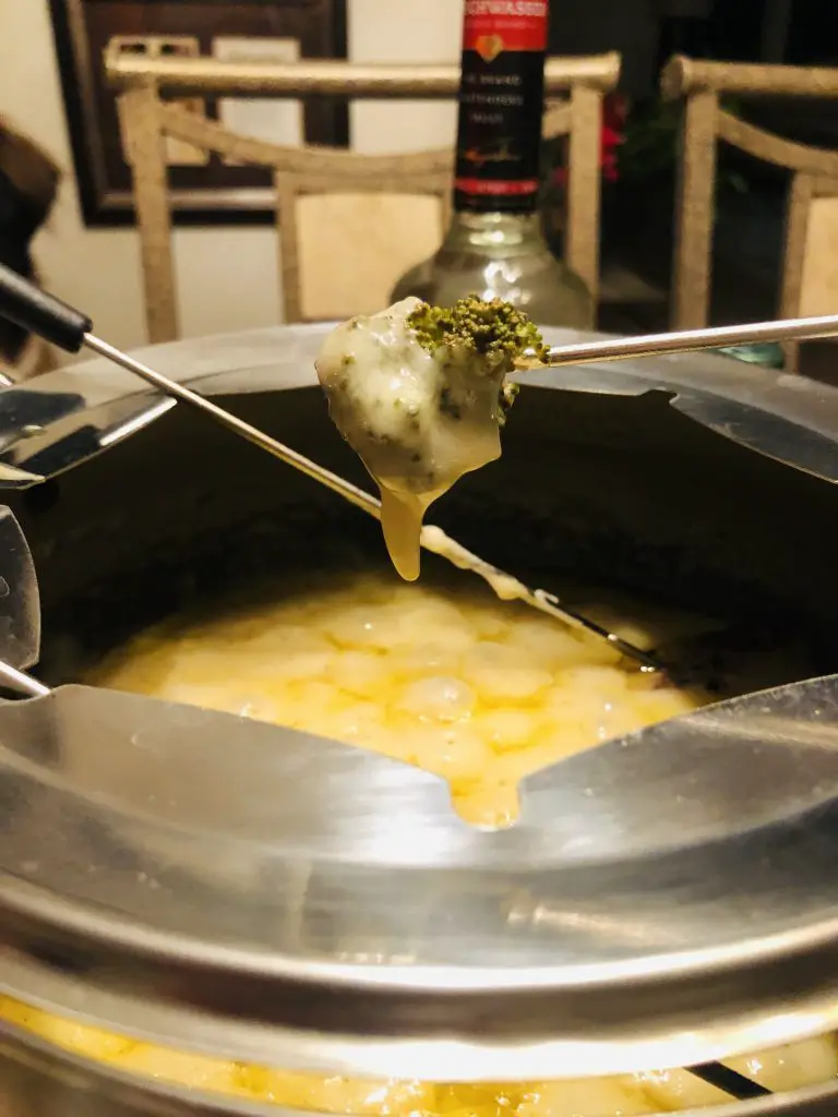 broccoli on a fondue fork dipped in cheese from a fondue pot