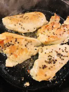 Chicken breasts sizzling in a cast iron pan seasoned with salt and coarse pepper