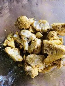 Small pieces of cut up cauliflower coated with a spice mixture in a glass bowl