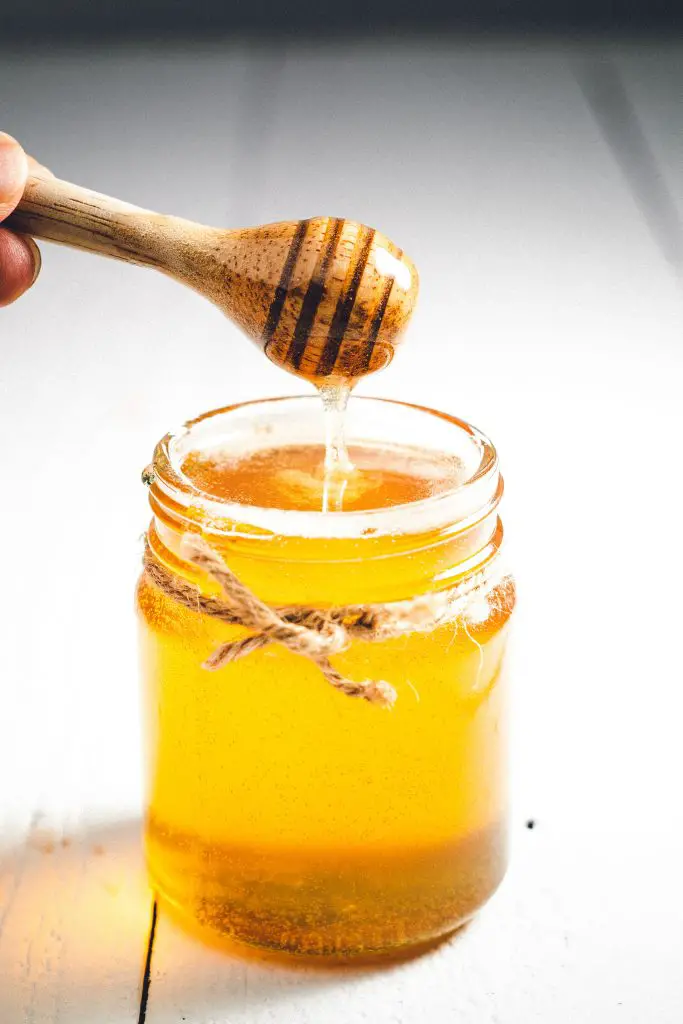 Jar of honey with a honey dipper poised above it