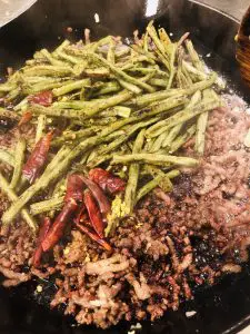 crispy ground pork, minced garlic and ginger, ground sichuan peppercorn, charred long beans, dried Asian Chilies and sauce in a cast iron skillet
