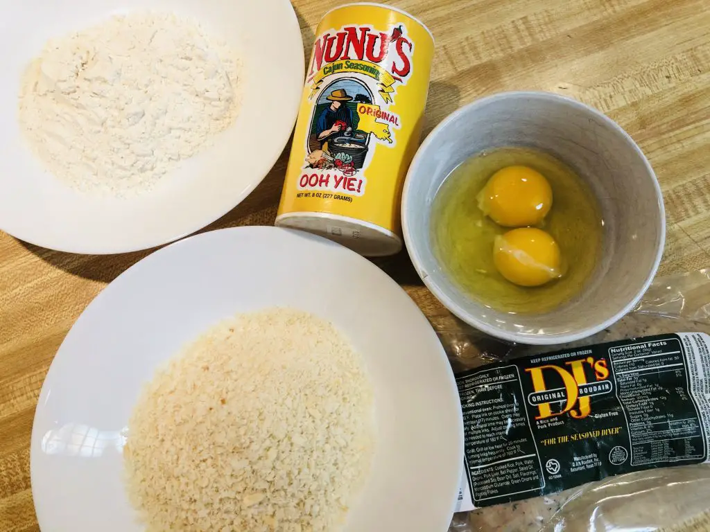Boudin sausage, panko in a white bowl, flour in a white bowl, nunu's cajun seasoning, 2 eggs in a white bowl