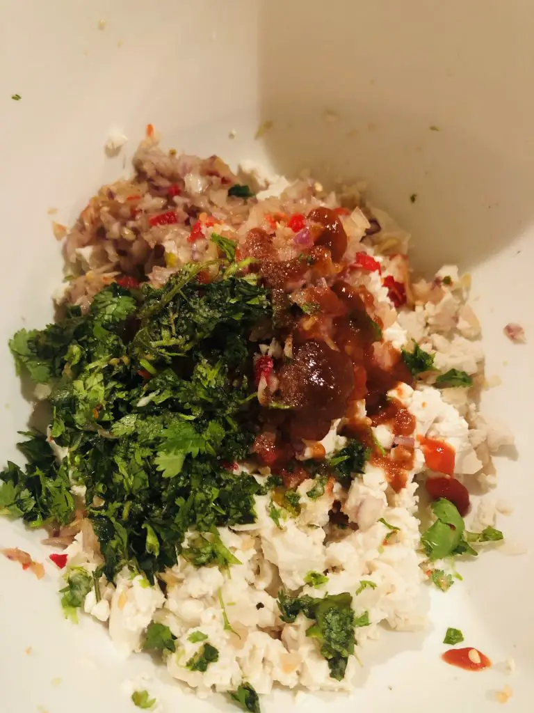 Crumbled up tofu, minced Thai chilis, Thai basil, cilantro and shallot in a white bowl with sriracha sauce 