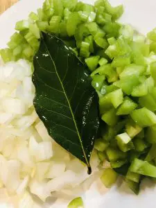 Diced onion, celery, and green bell pepper with a bay leaf on top