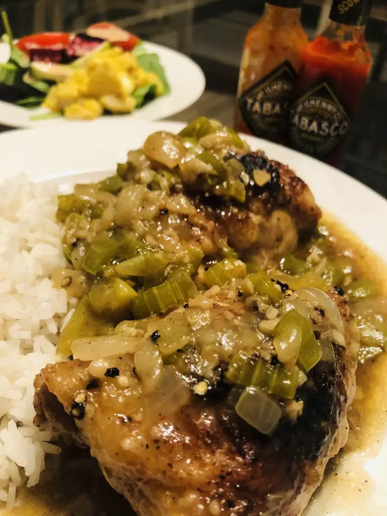 Cajun Smothered Chicken served with white rice on a plate with bottles of Tabasco in the background and a salad