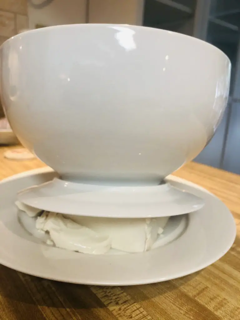 Heavy white bowl on top of a small plate placed on top of tofu on a white plate