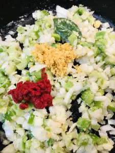 Diced green bell pepper, onion, and celery with bay leaf, minced garlic, and tomato paste