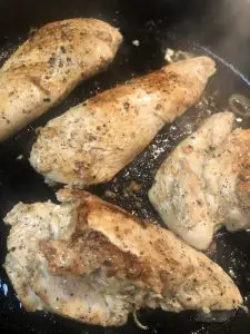 Browning chicken breasts in a cast iron skillet with olive oil