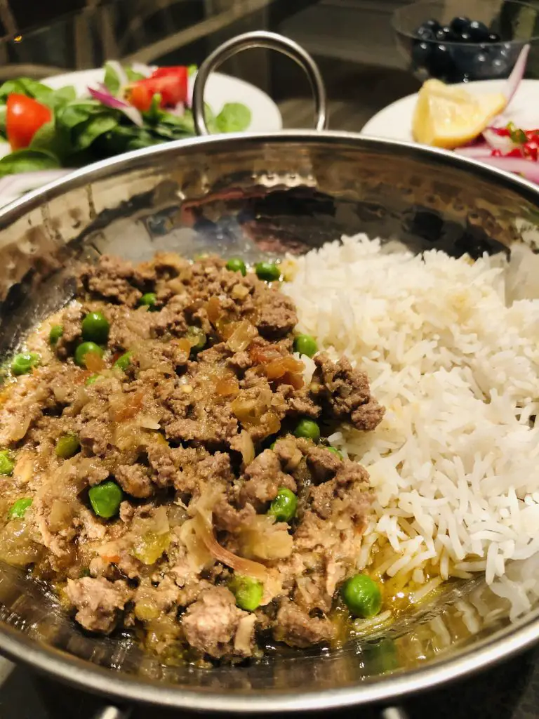 Keema do pyaza and rice in a silver bowl, with onion salad and spinach salad on white plates in the background 