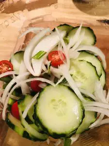 sliced cucumbers, onions, cherry tomatoes, and green onions in a glass bowl