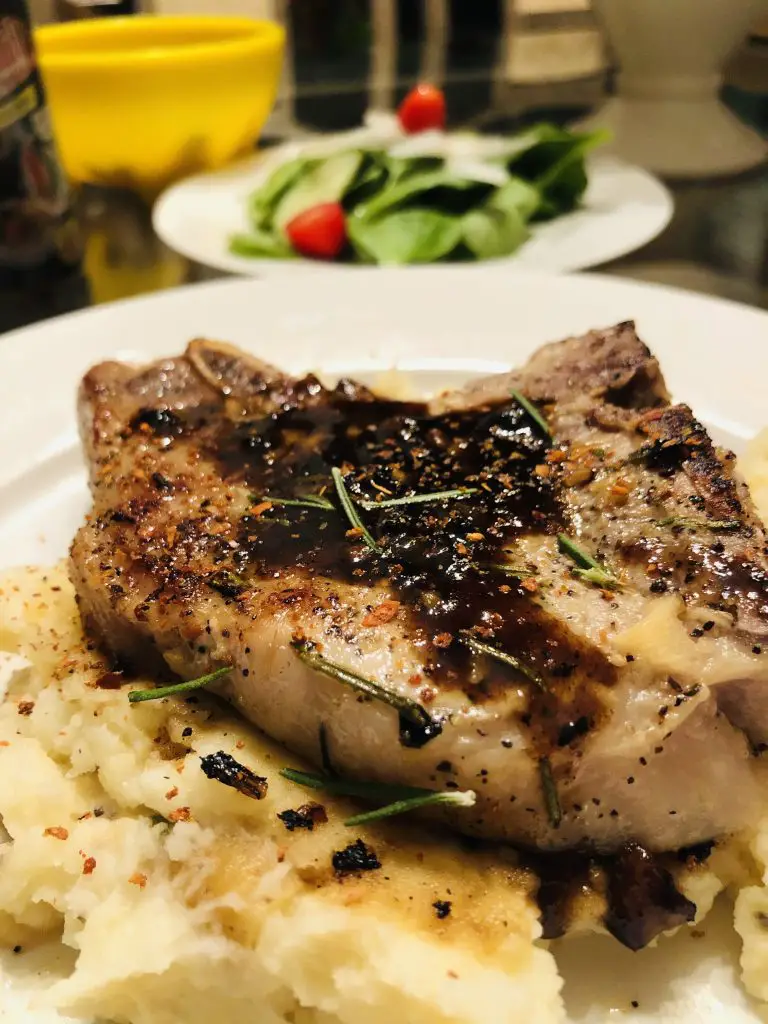 Pork chop with rosemary and caramelized sauce and mashed potatoes with a salad in the background