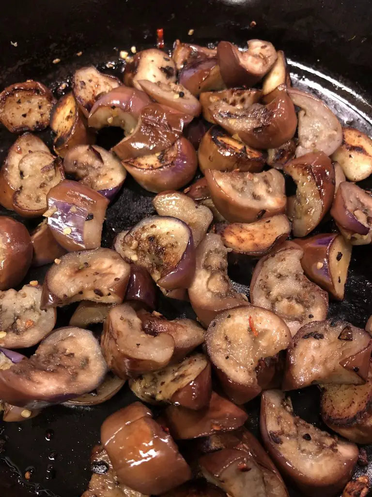 cut up pieces of Japanese eggplant being browned and cooked in a cast iron pan