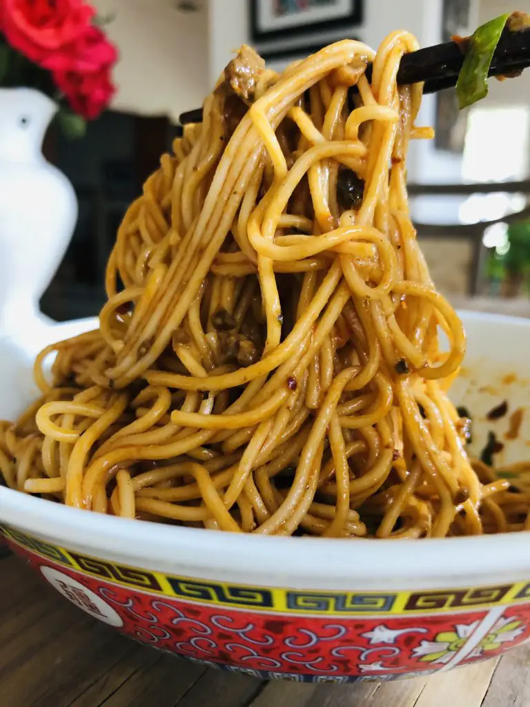 Dan dan noodles in a bowl with chopsticks holding up some of the noodles