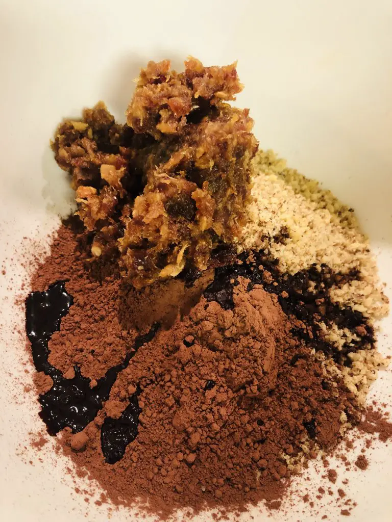 Cacao powder, walnuts, coffee concentrate, and dates in a white mixing bowl