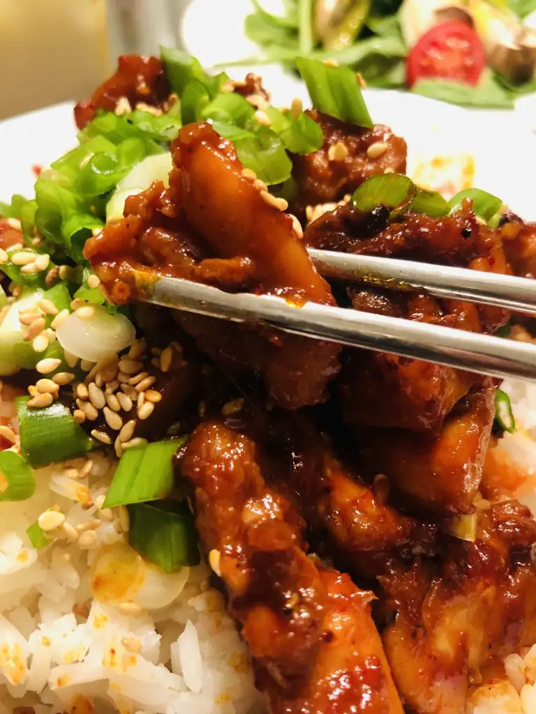 Spicy Chicken Bulgogi With rice garnished with green onions and sesame seeds and chopsticks holding a piece of bulgogi