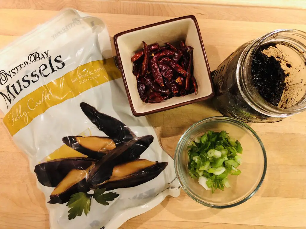 A package of frozen mussels, some black bean sauce in a glass jar, sliced green onions and dried Asian chilies 