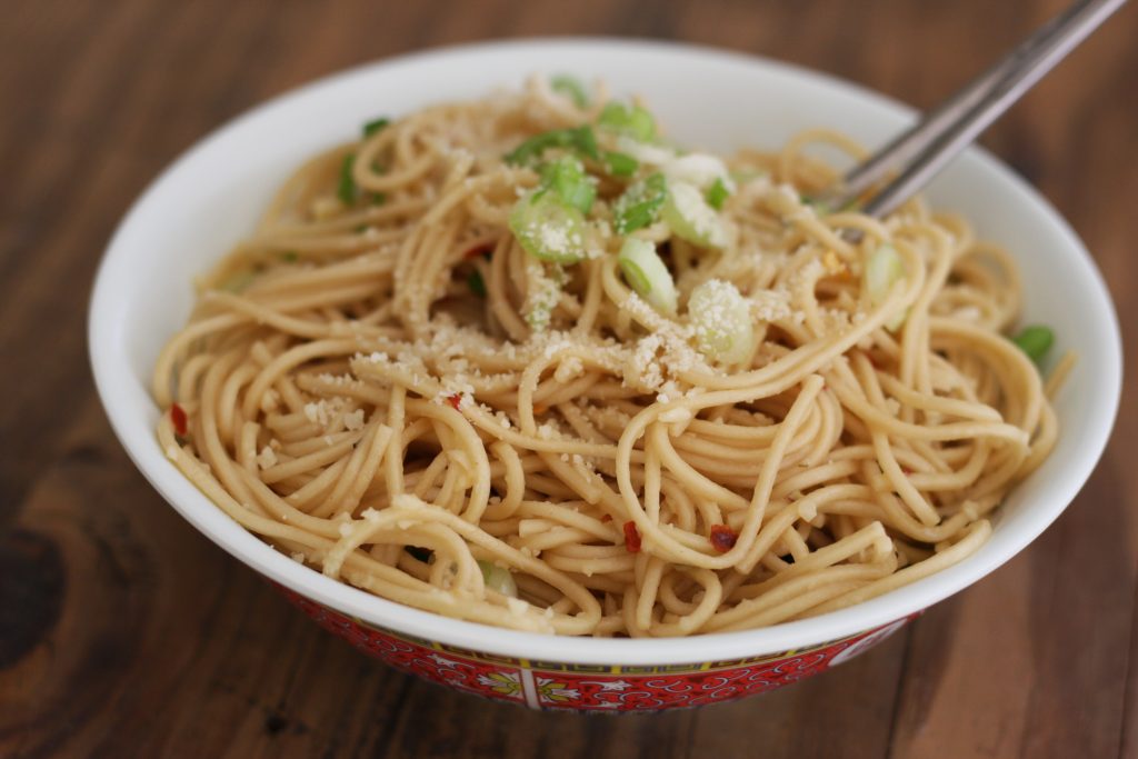 Asian noodles topped with parmesan and green onions in a bowl with chopsticks
