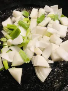 Pieces of cut up onion and green onion in a cast iron skillet