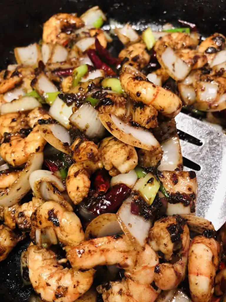 Shrimp with black bean sauce in a cast iron pan with a spatula on the side 