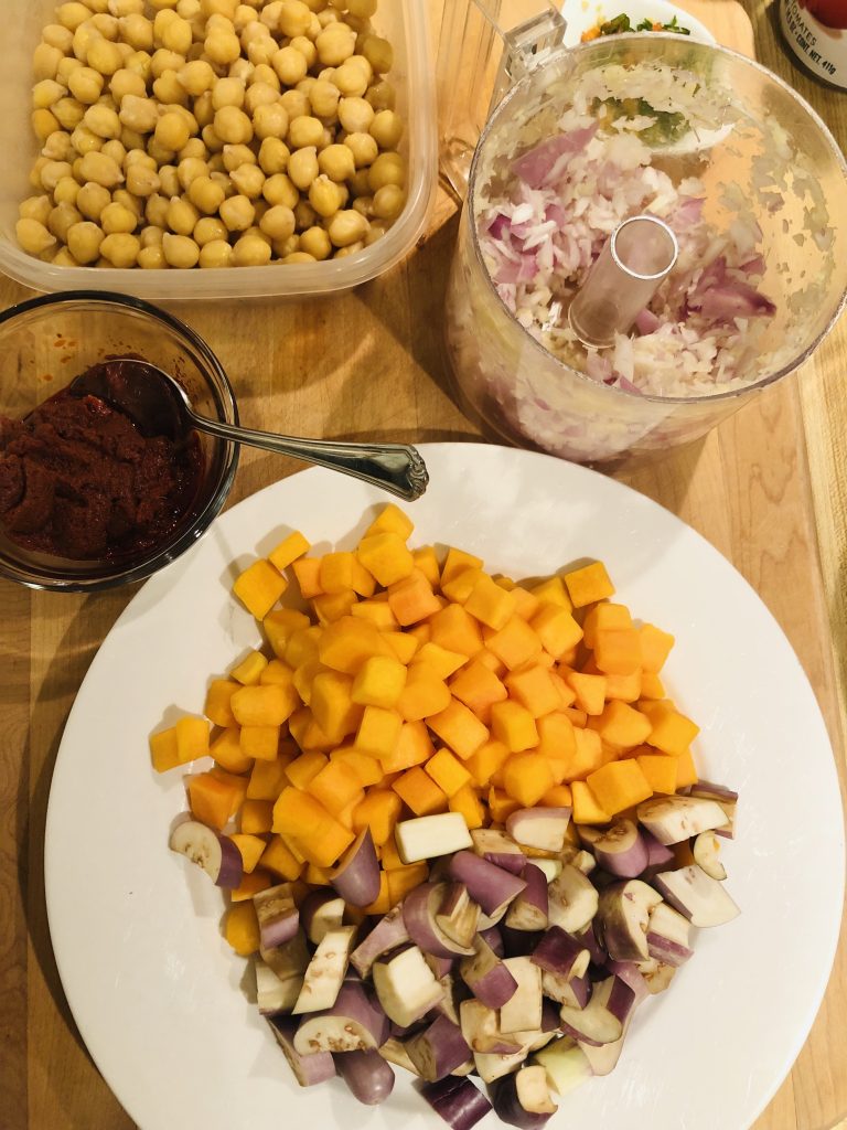 diced butternut squash and eggplant on a white plate, minced shallot and ginger in a food processor, panang curry paste in a glass bowl with a spoon, and chickpeas in a plastic container