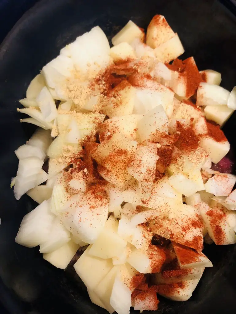 diced onions and potatoes in a slow cooker with paprika sprinkled on top