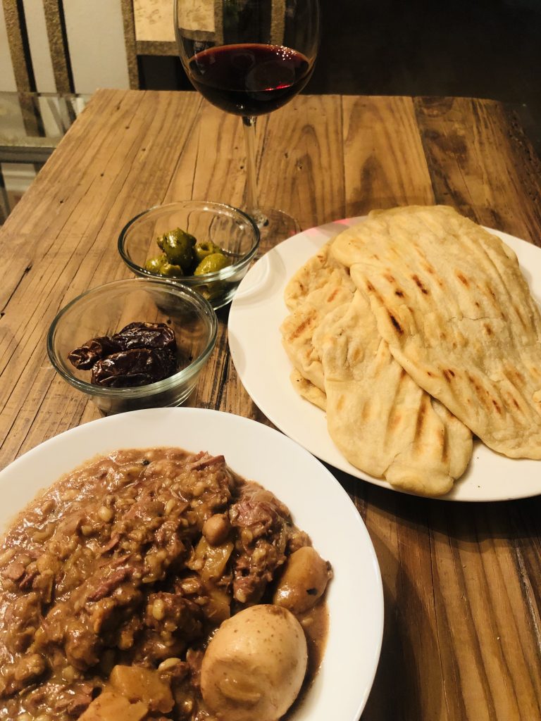 Cholent with homemade bread, glass bowls filled with olives and dates and a glass of red wine