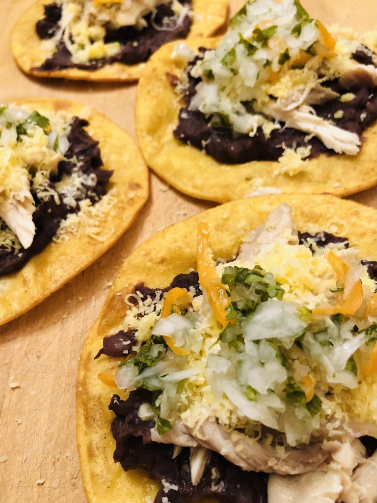 Several Belizean garnaches corn tortilla topped with refried beans, chicken, shredded cheese, and hot pepper onion sauce
