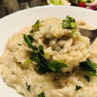 Chicken Risotto in a white bowl garnished with parsley with salad in the background