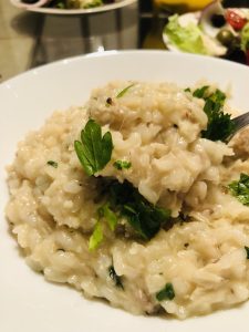 Chicken Risotto in a white bowl garnished with parsley with salad in the background