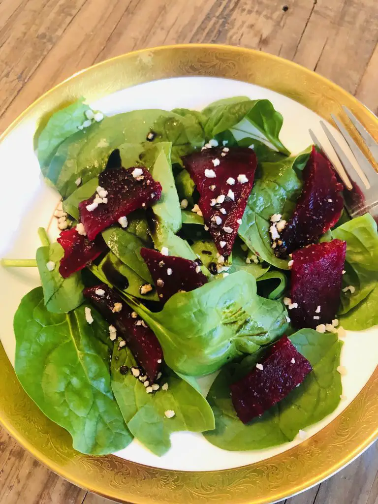 Roasted Beets and Spinach Salad in a gold rimmed bowl with a fork on the side