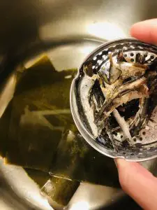 anchovies in an anchovy strainer and kelp in water in a pot in the background