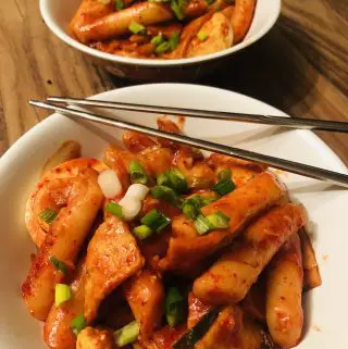 2 bowls of korean spicy rice cakes garnished with green onions and a pair of silver chopsticks laying across one of the bowls