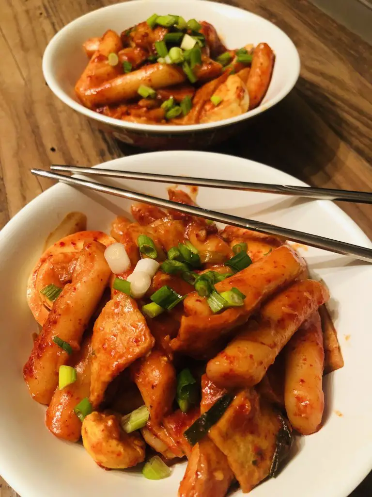 2 bowls of korean spicy rice cakes garnished with green onions and a pair of silver chopsticks laying across one of the bowls