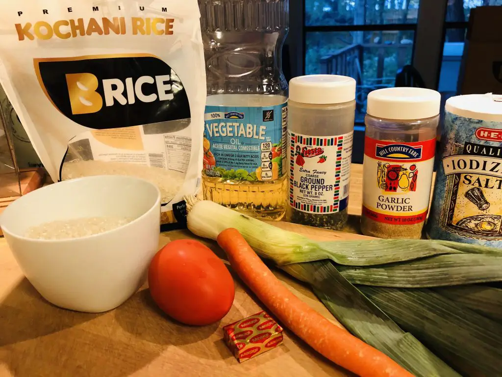 Bag of B Rice Kochani rice, rice in a white bowl, tomato, carrot, leek, vegetable oil, pepper, garlic powder, salt, and Maggi bouillon cube