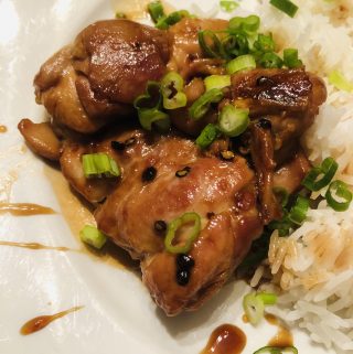 Teriyaki Chicken garnished with green onions and Nanami Togarashi served with rice on a white plate