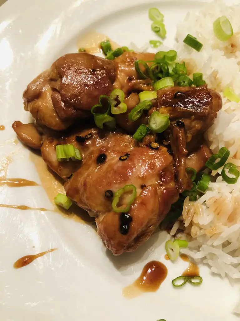 Teriyaki Chicken garnished with green onions and Nanami Togarashi served with rice on a white plate