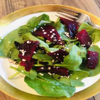roasted beets and spinach salad in a gold rimmed bowl with a fork