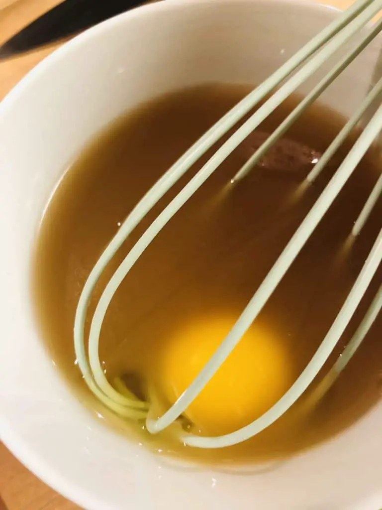 Egg and turkey broth in a white bowl with a whisk