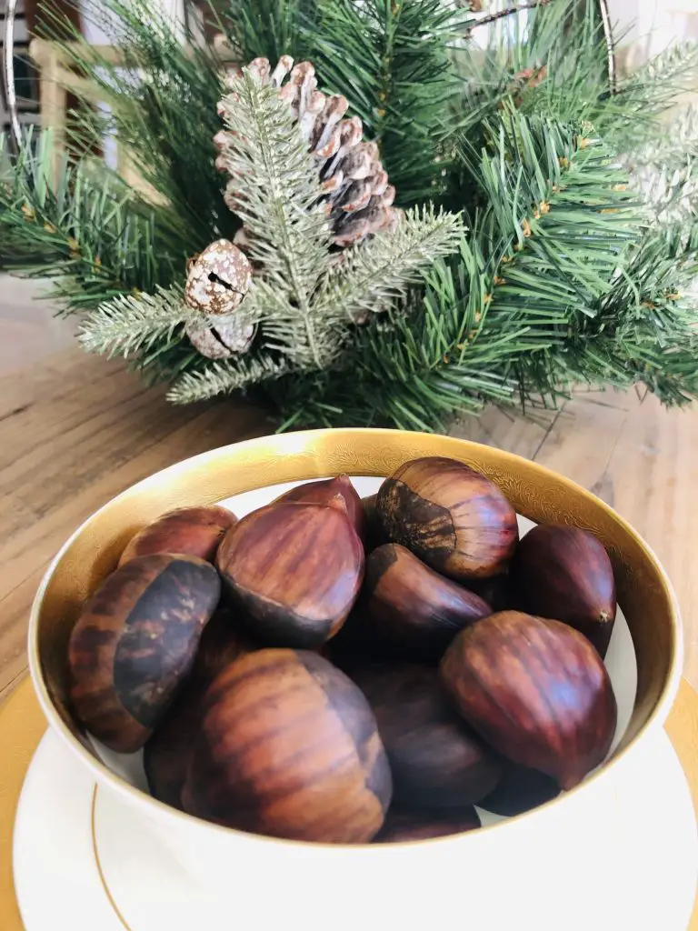 chestnuts in a gold rimmed bowl with greenery behind it
