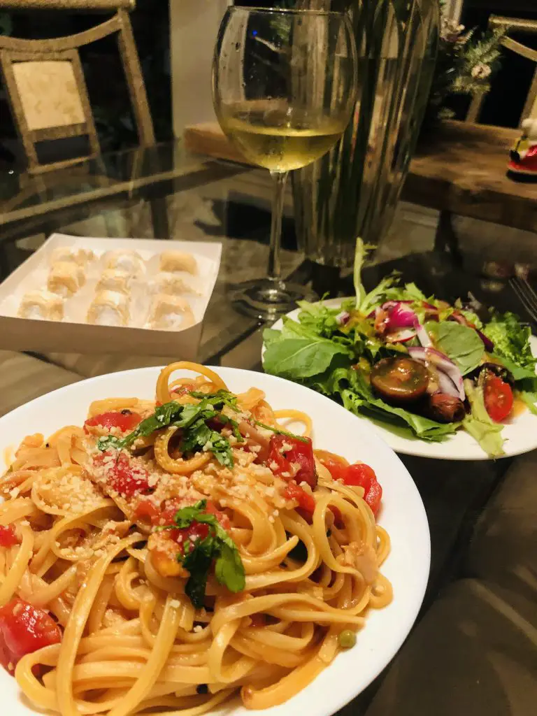 A plate of linguine with red clam sauce, along with some salad, a box of amaretti, and a glass of wine in the background