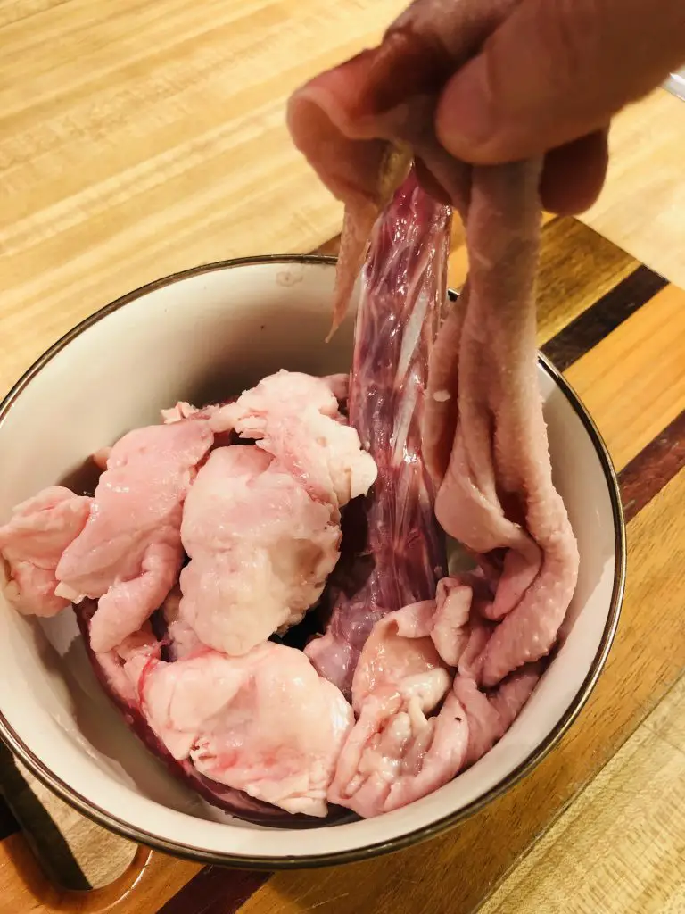 Giblets from a goose and excess fat which has been removed and placed in a bowl with someone holding up the excess fat