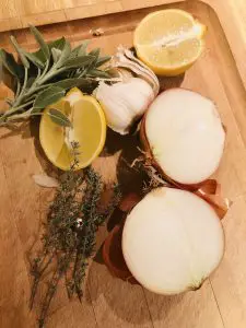 halved lemon, halved onion, head of garlic, sage, and thyme on a wooden board