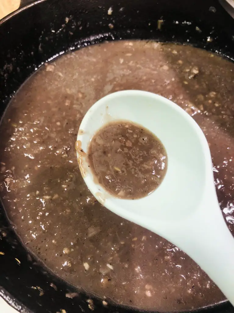 Goose Giblet Gravy in a skillet with some of the gravy in a blue spoon 
