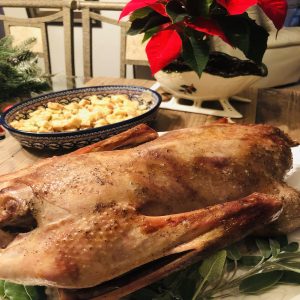 Roasted Goose on a white serving tray with sage and onion stuffing and a poinsettia in the background