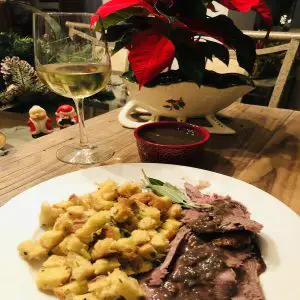 Roast goose and sage and onion on a white plate with some sage, glass of wine and poinsettia in the background