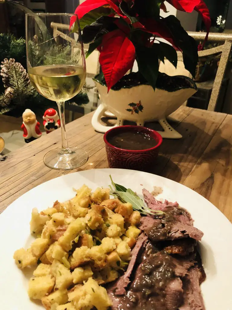 Roasted Goose With sage and onion stuffing on a white plate with a glass of wine and a poinsettia in the background